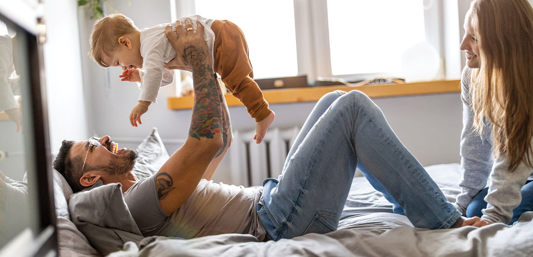 man playing with his son on bed and his wife next to him