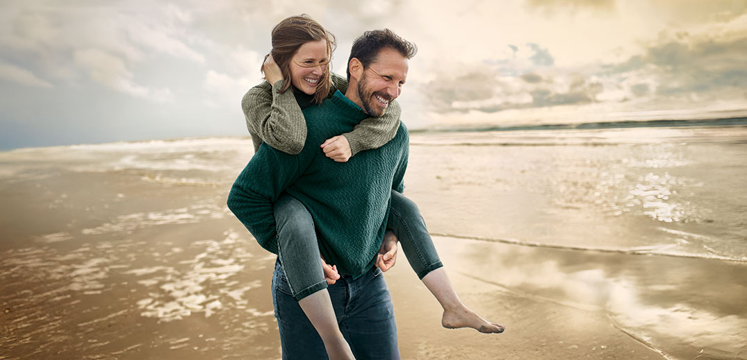 Couple enjoying a playful piggyback ride on a sandy beach at sunset