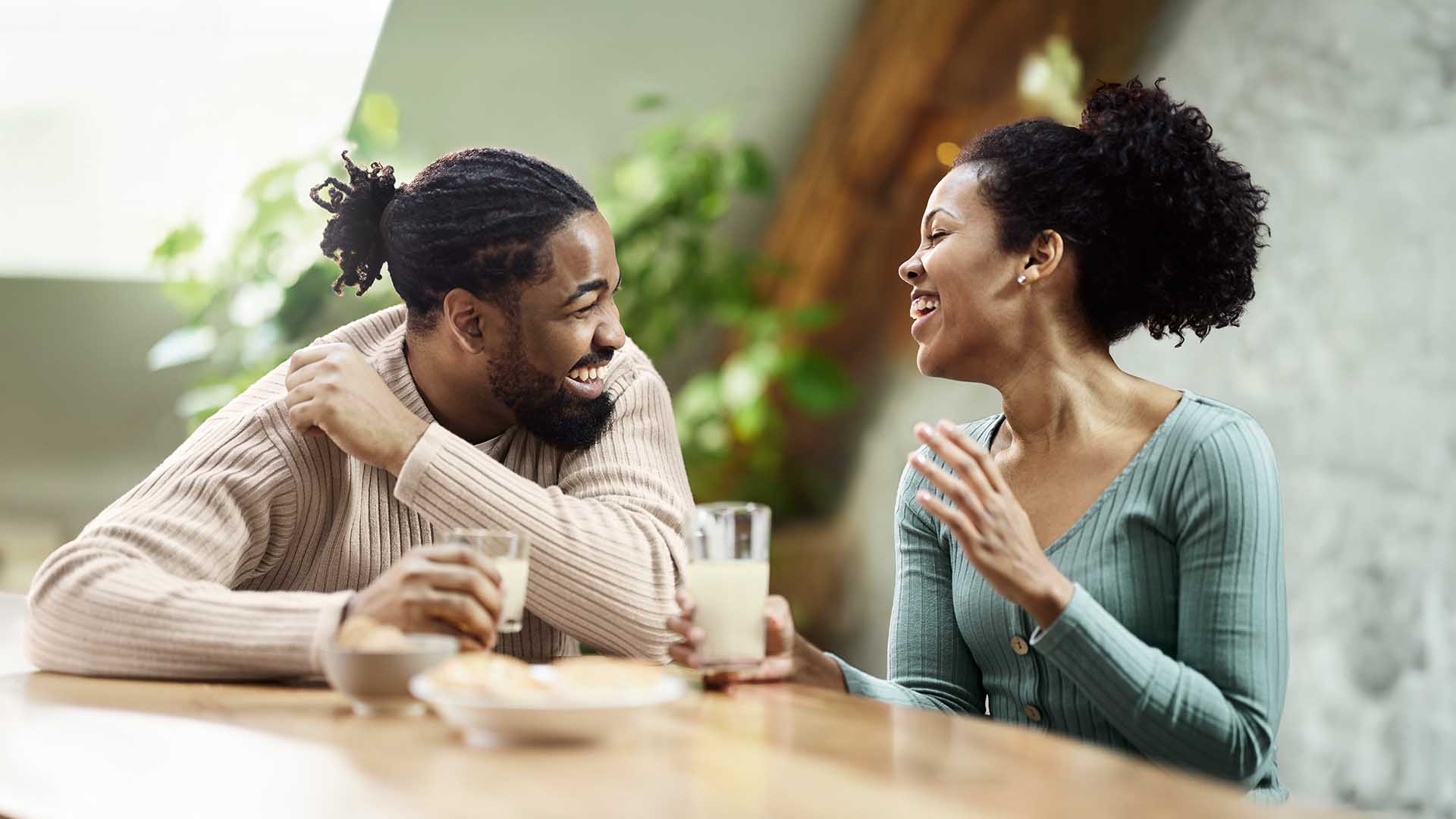 Two people sitting at a table and talking while holding drinks in a bright indoor setting