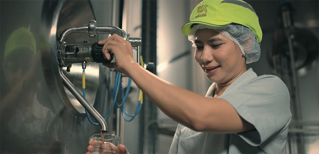 Factory worker collecting product sample from stainless steel processing equipment
