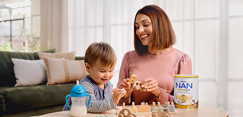 Parent and child playing with toys beside NAN infant formula can