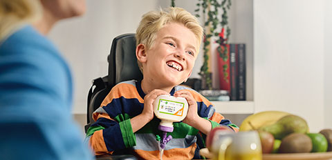 Child holding a nutritional drink bottle at a table with fruit