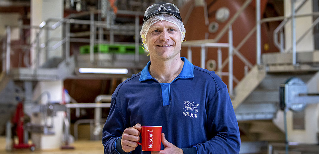 Factory worker in safety gear walking through a modern coffee production facility
