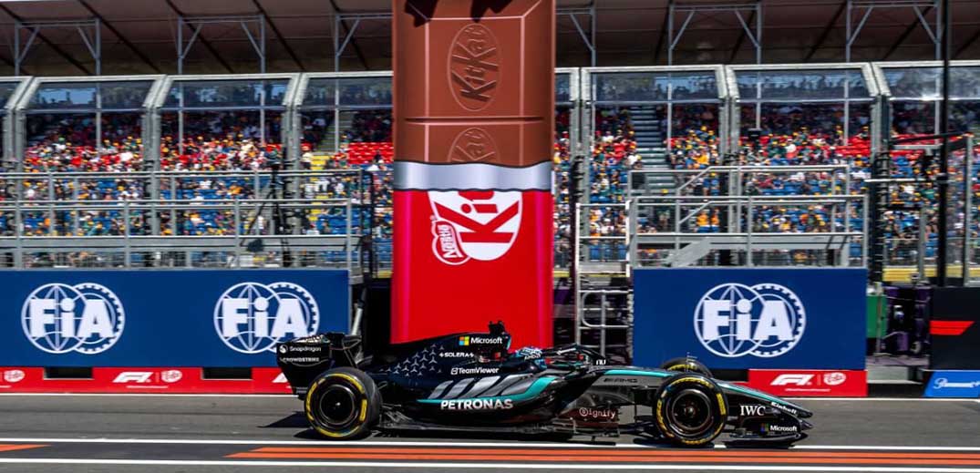 Formula 1 car driving past a giant KitKat bar at a race track event