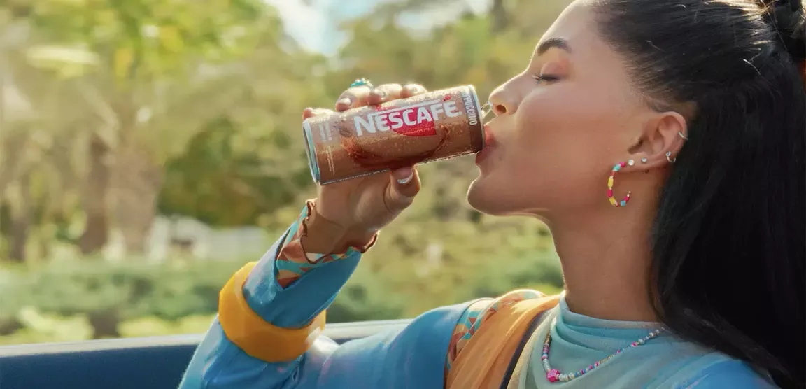 Person drinking Nescafé iced coffee from a can while traveling in a car
