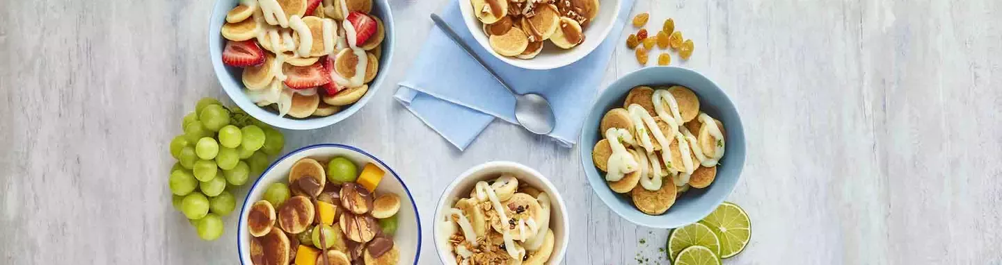 Five bowls of mini pancakes with fresh fruit