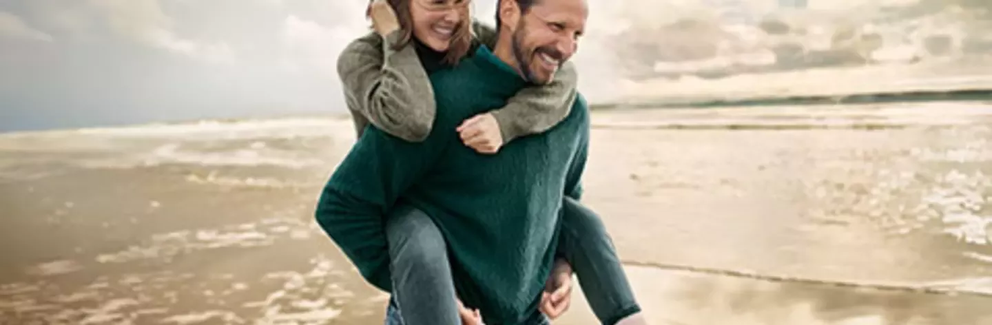 Couple enjoying a playful piggyback ride on a sandy beach at sunset