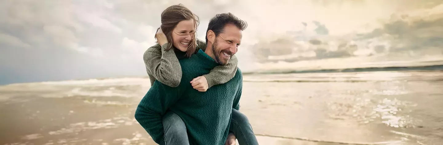 Couple enjoying a playful piggyback ride on a sandy beach at sunset
