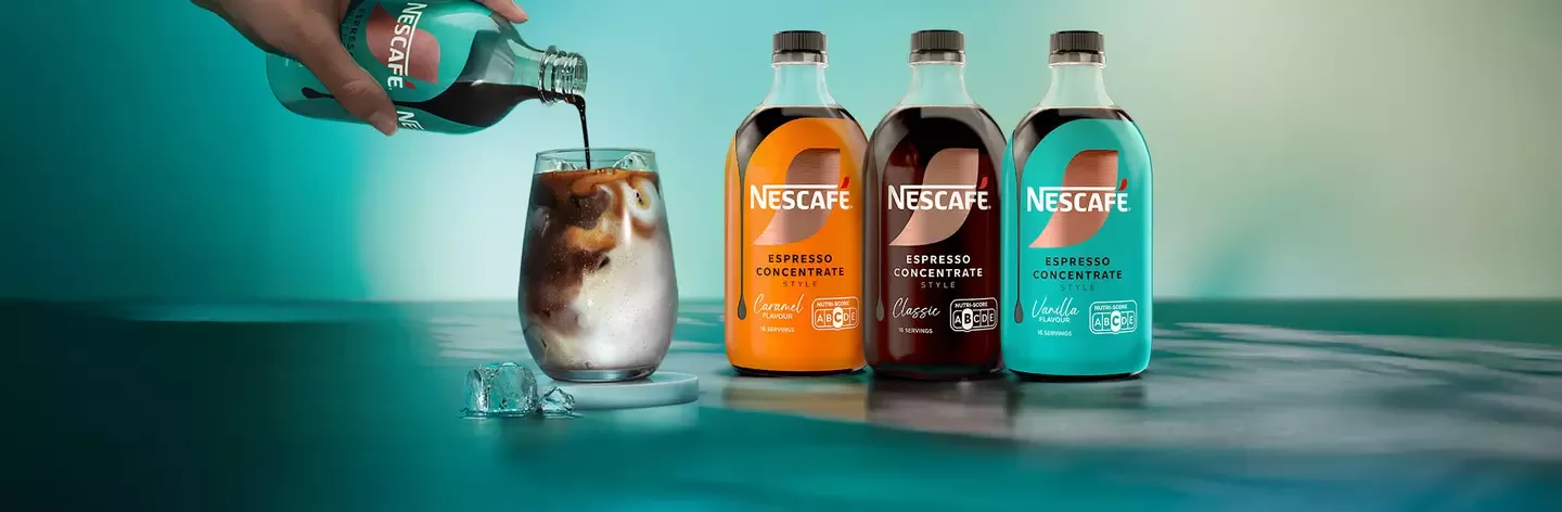 Nescafé Espresso Concentrate bottles beside an iced coffee glass as espresso concentrate is poured