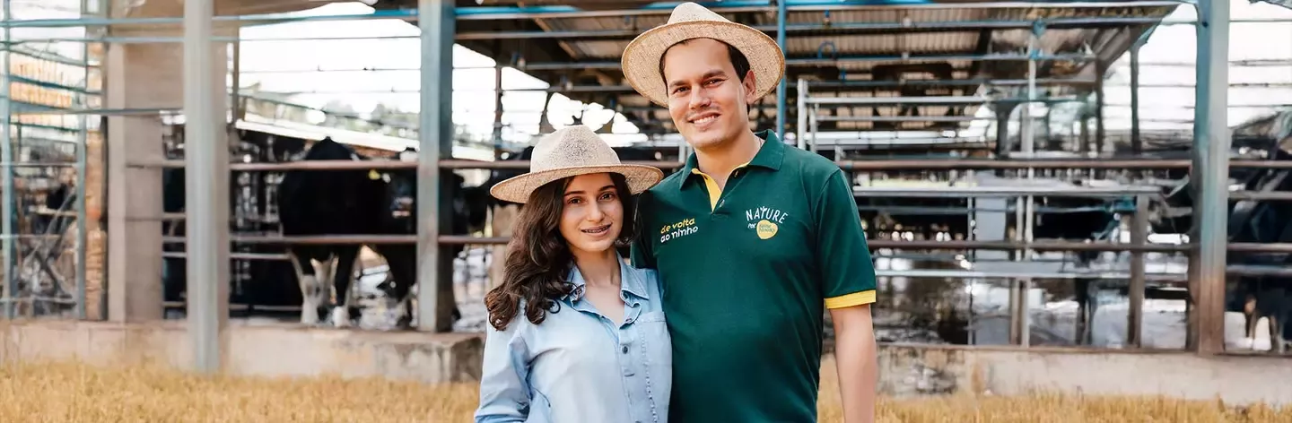 Two people wearing straw hats standing in a dairy farm with cows and feeding structures behind