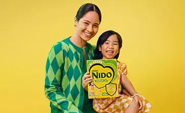 Mother sitting with little daughter holding NIDO product