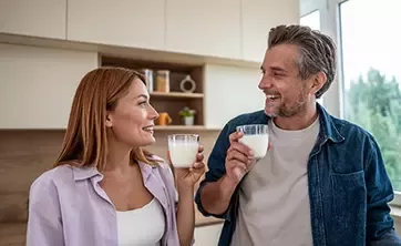 Adult couple holding glasses of milk together in a bright kitchen at home