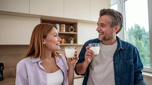 Adult couple holding glasses of milk together in a bright kitchen at home