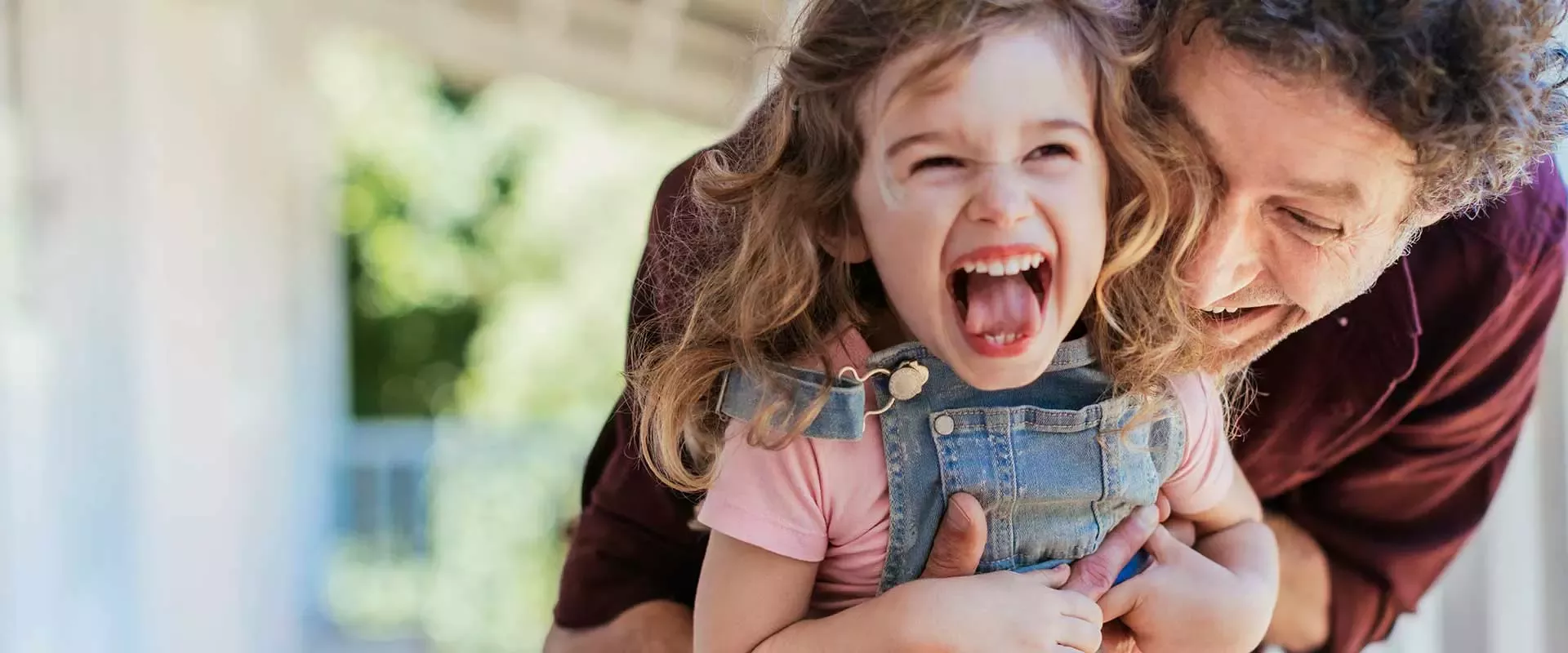 A smiling man, holding his young daughter who is laughing
