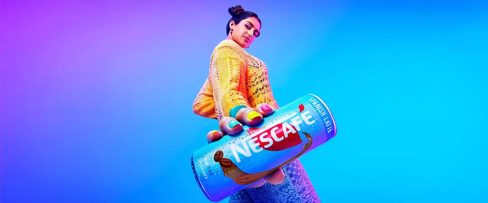 Young woman holding a large Nescafé can against a vibrant blue and purple background