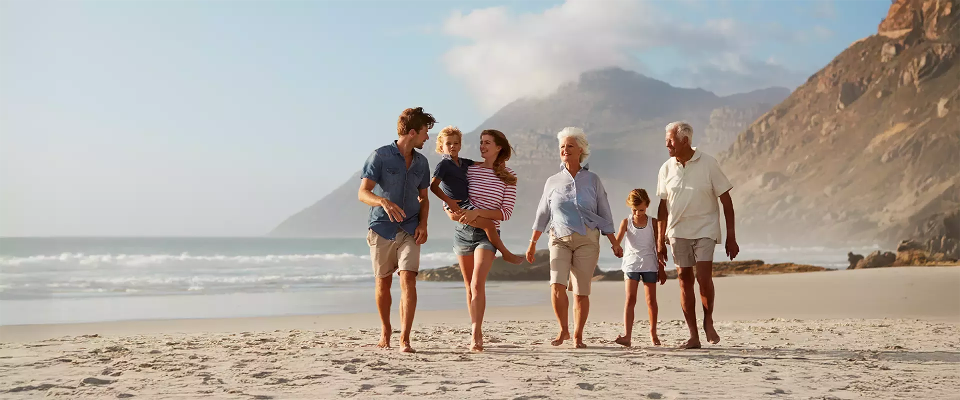 Multigenerational family walking together along a sandy beach with ocean and mountains