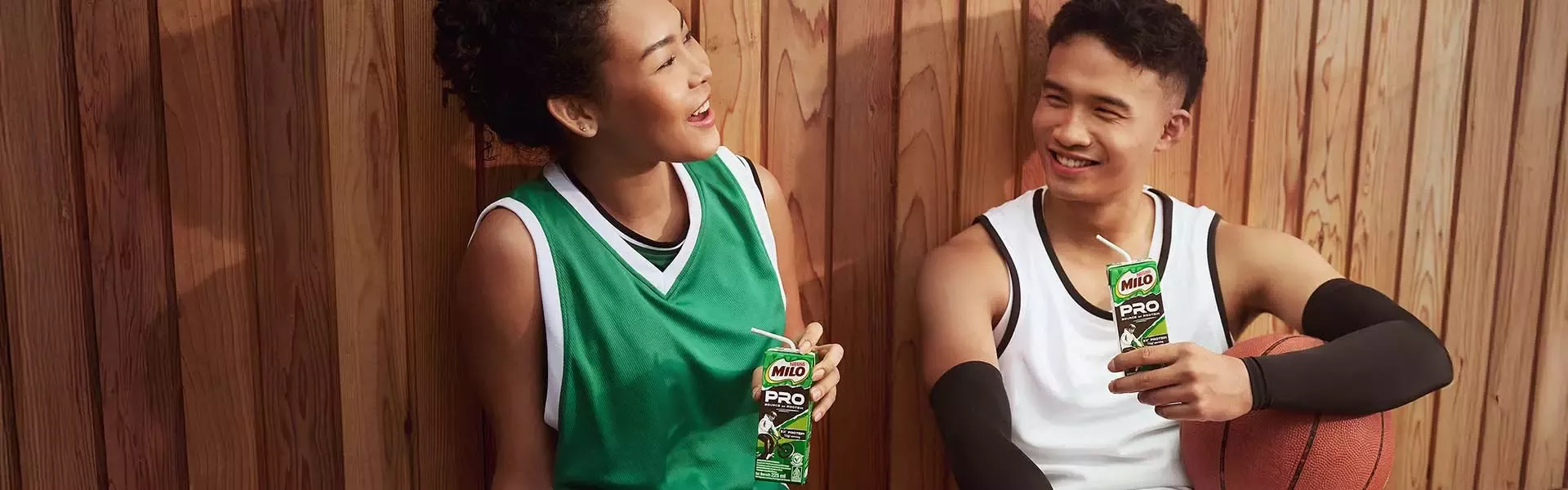 Two basketball players resting with Milo Pro drinks against a wooden wall