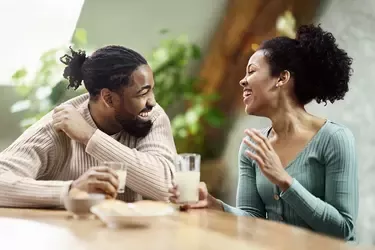 Two people sitting at a table and talking while holding drinks in a bright indoor setting