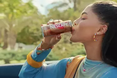 Person drinking Nescafé iced coffee from a can while traveling in a car