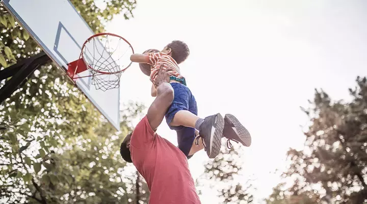 Kid lifted by parent in order to dunk a basketball