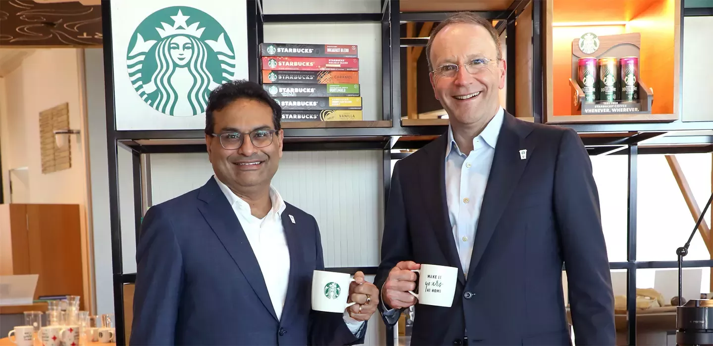 2 men drinking from mugs in front of starbucks sign