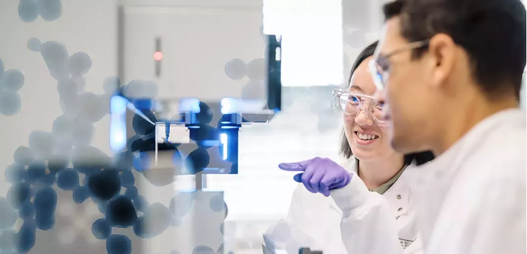 Two scientists in lab coats engage in a discussion, pointing at advanced lab equipment with molecular visuals in the background.