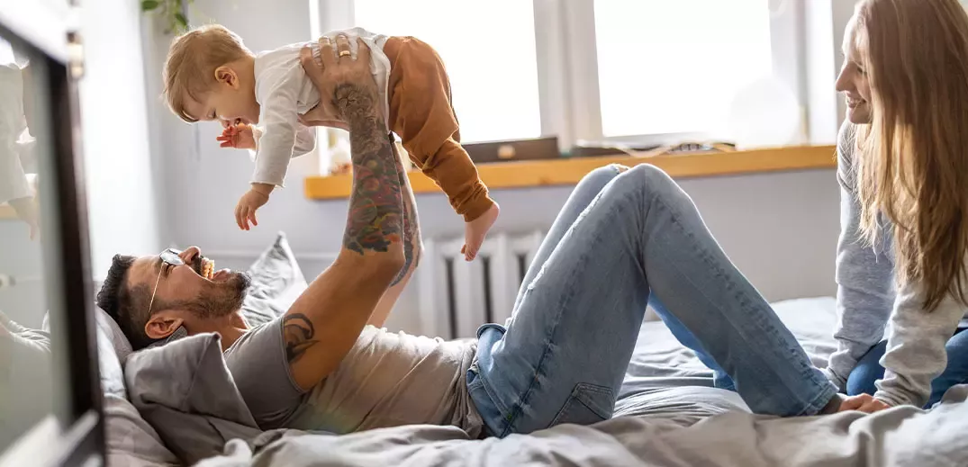 man playing with his son on bed and his wife next to him