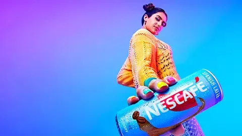 Person holding a Nescafé Spanish Latte can against a blue‑purple background