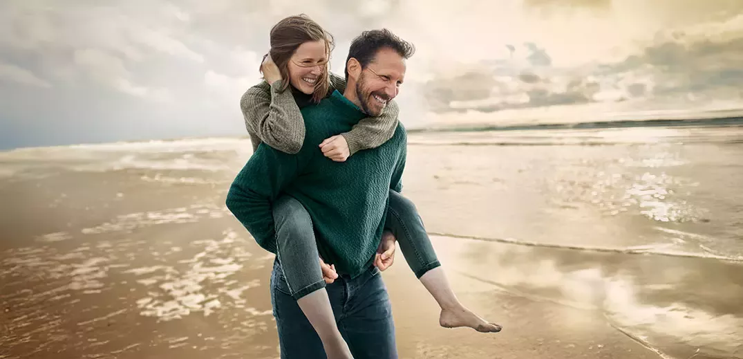 Couple enjoying a playful piggyback ride on a sandy beach at sunset