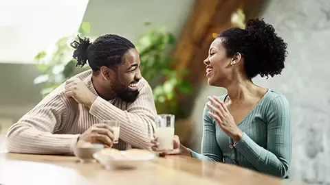 Two people sitting at a table and talking while holding drinks in a bright indoor setting