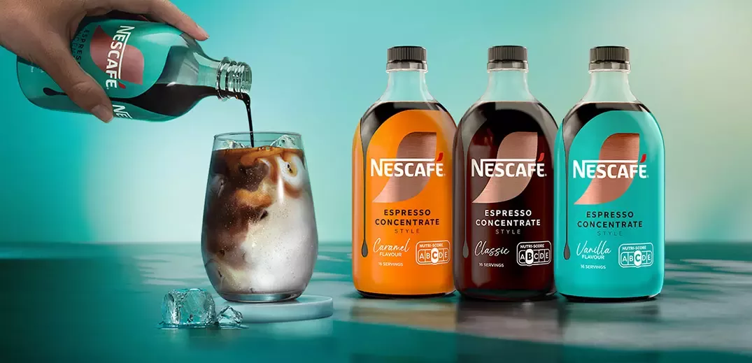 Nescafé Espresso Concentrate bottles beside an iced coffee glass as espresso concentrate is poured