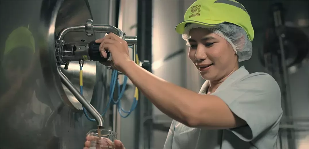 Factory worker collecting product sample from stainless steel processing equipment