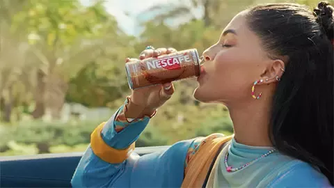 Person drinking Nescafé iced coffee from a can while traveling in a car